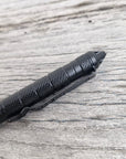 A close-up of the Op Gear Tactical Pen - Recon with a textured grip, resting on a weathered wooden surface—an essential everyday carry survival tool.