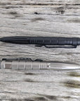Two Op Gear Tactical Pen - Recon models, one black and one silver, lie parallel on a weathered wooden surface. Both feature textured grips and pointed ends for dependable self-defense in daily use.