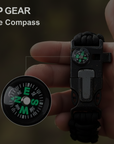 Hand holding a black compass with visible brand 'OP GEAR' on a blurred background