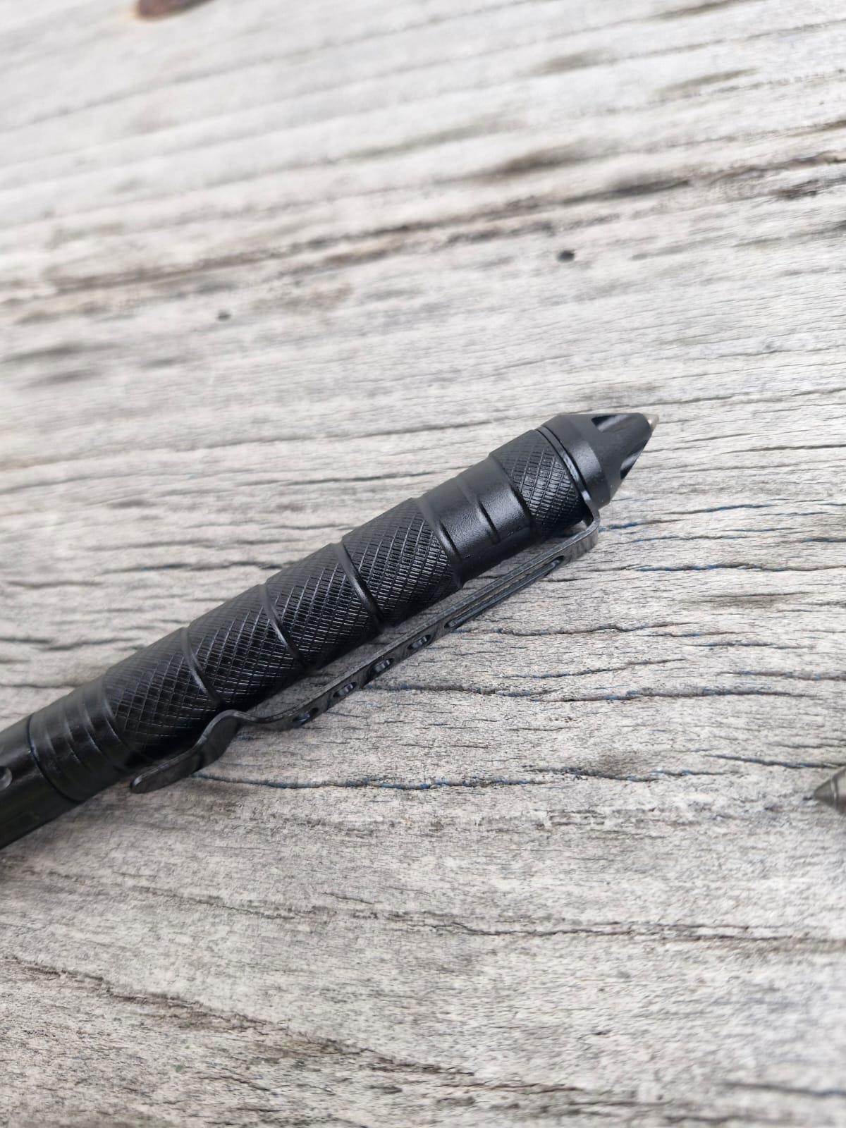 A close-up of the Op Gear Tactical Pen - Recon with a textured grip, resting on a weathered wooden surface—an essential everyday carry survival tool.