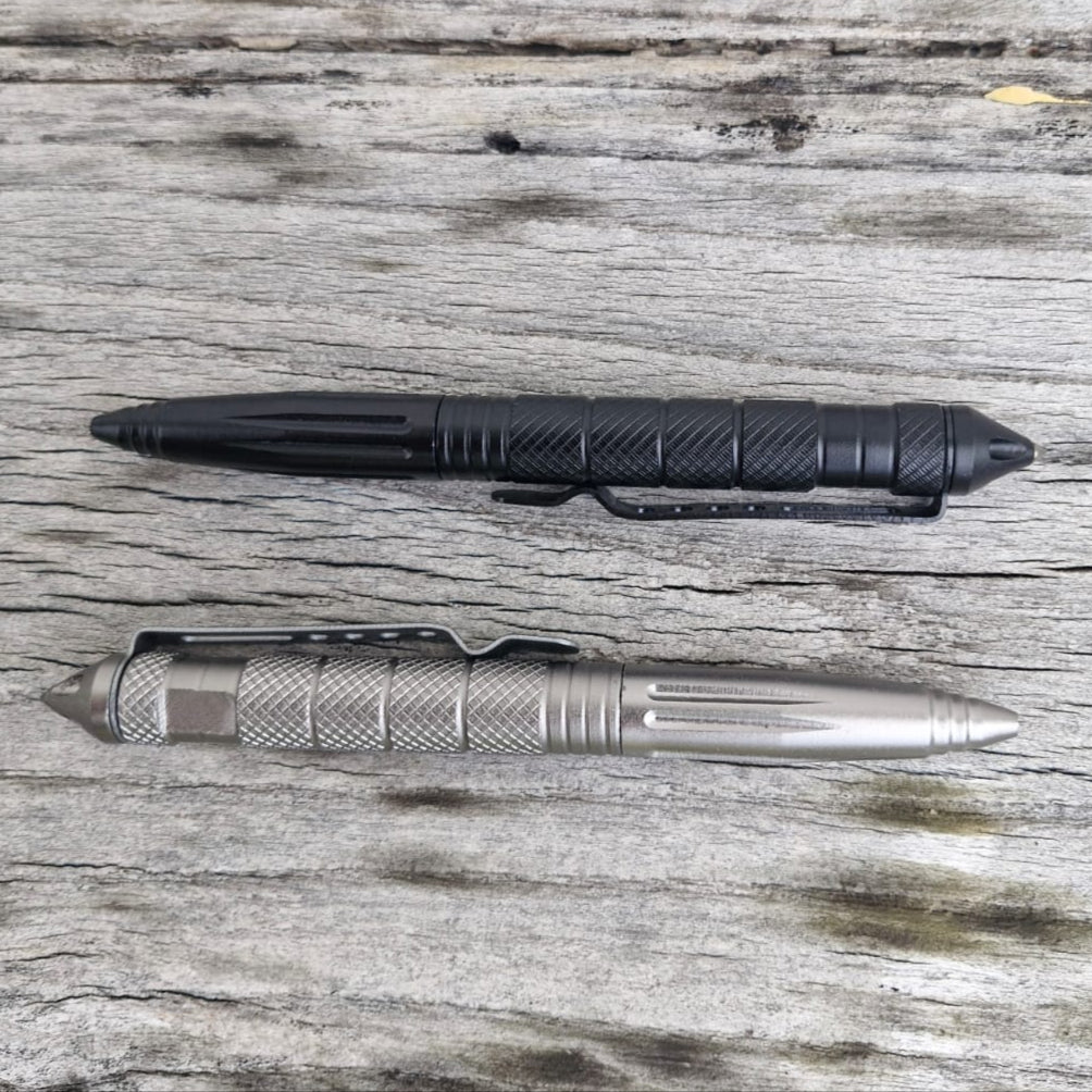 Two Op Gear Tactical Pen - Recon models, one black and one silver, lie parallel on a weathered wooden surface. Both feature textured grips and pointed ends for dependable self-defense in daily use.